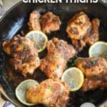 Blackened Chicken Thighs garnished with lemon in cast iron pan.