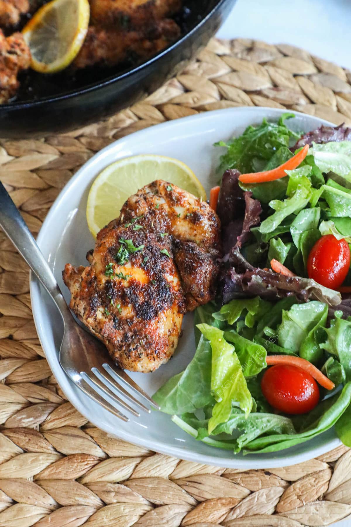 Blackened chicken thighs served with salad on a plate for an easy high protein dinner idea.