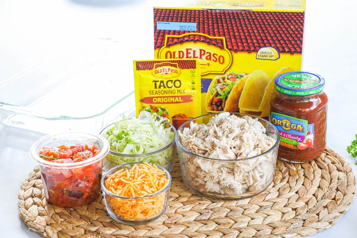Ingredients to make baked chicken tacos including shredded chicken, lettuce, cheese, salsa, and pico de gallo