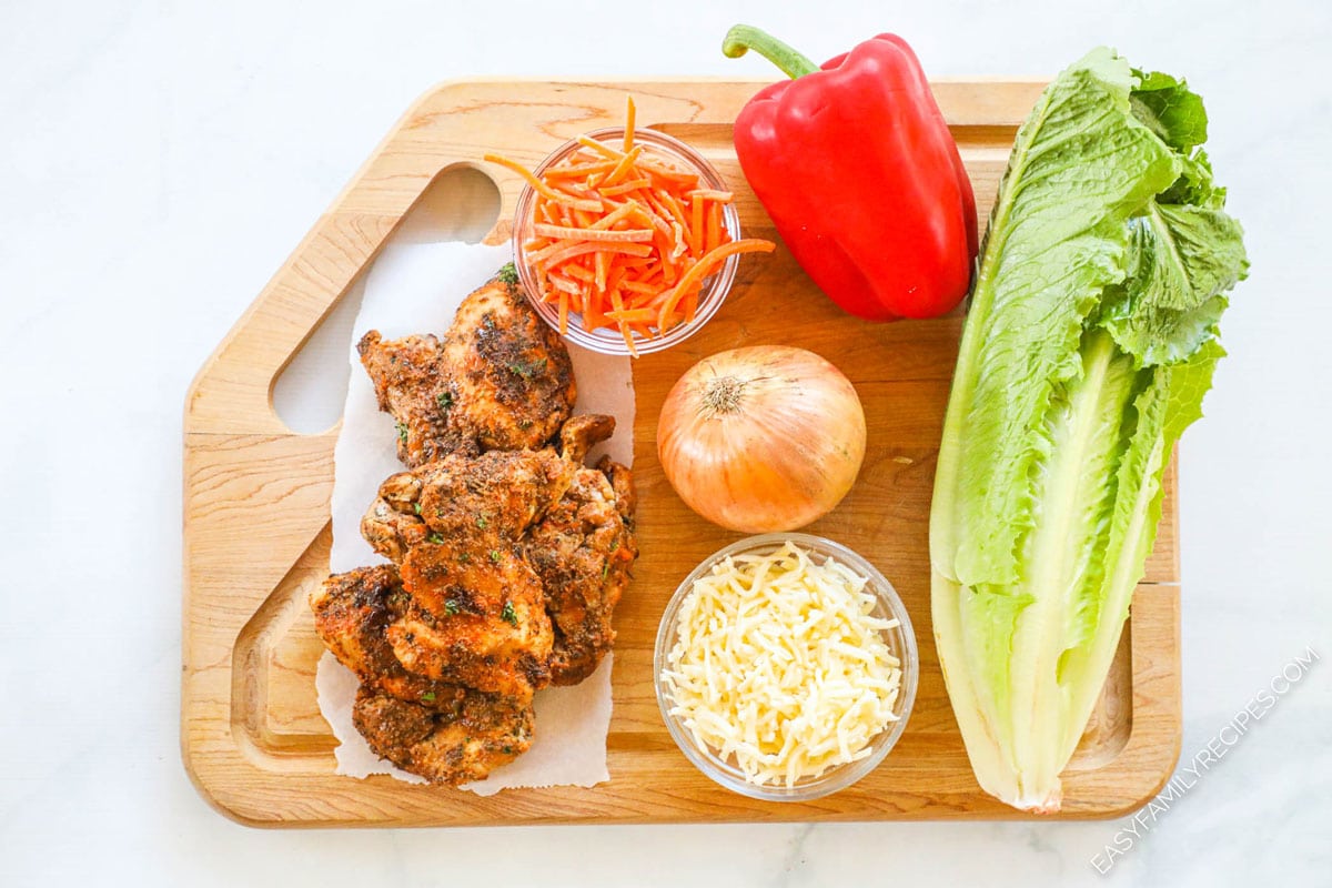 Ingredients for making blackened chicken salad including blackened chicken breast, shredded carrots, sliced bell pepper, shredded cheese, thinly sliced onion.