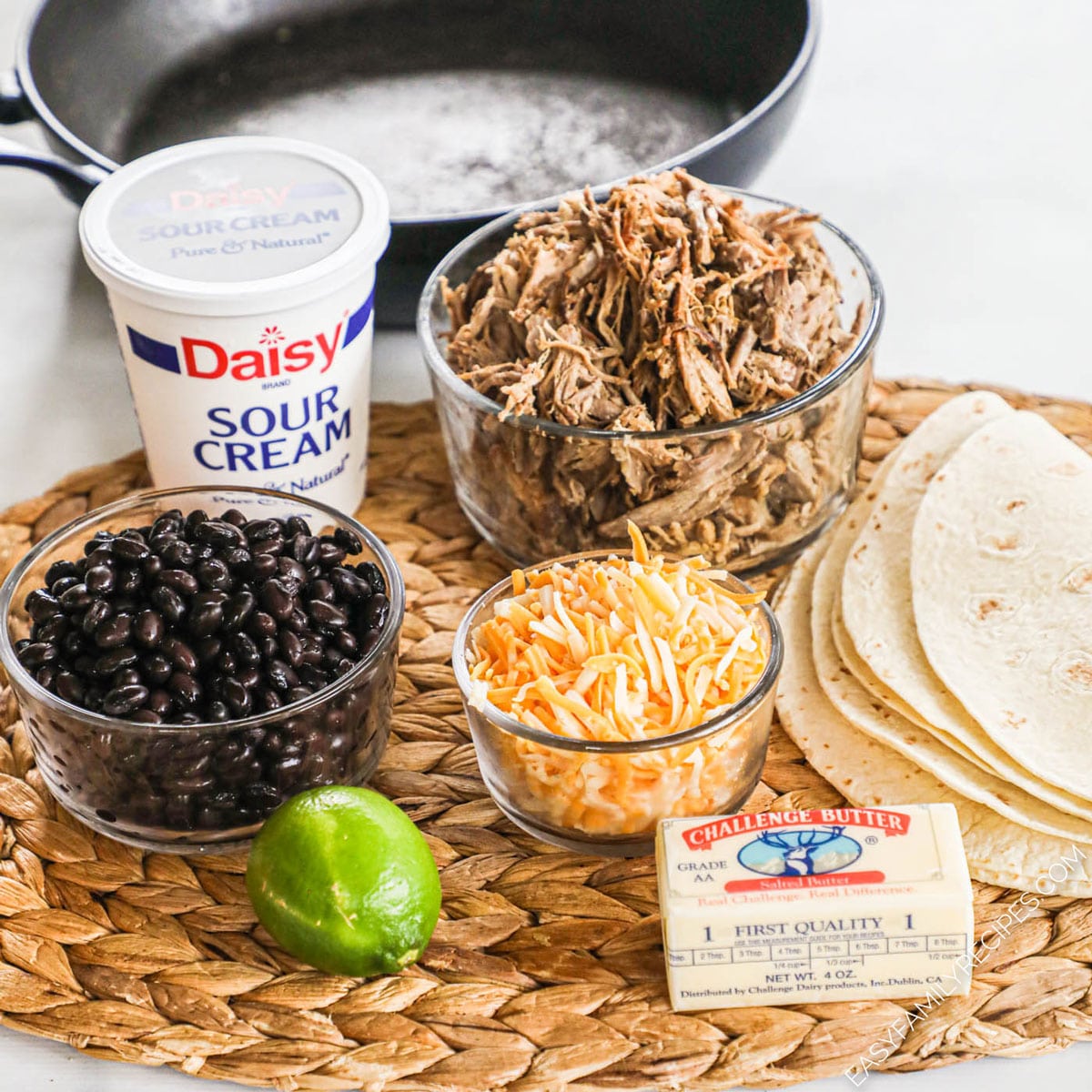 Ingredients for carnitas quesadillas including leftover carnitas, sour cream, black beans, shredded Colby jack cheese, lime, butter, and large flour tortillas