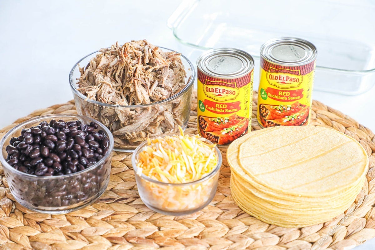 ingredients for recipe: black beans, pork carnitas, shredded cheese, 2 cans of red enchilada sauce, and stack of corn tortillas.