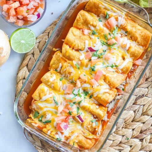 Rolled pork carnitas enchiladas in a pan with red enchilada sauce and cheese