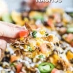 close up of hand picking up nachos with all ingredients loaded on chip