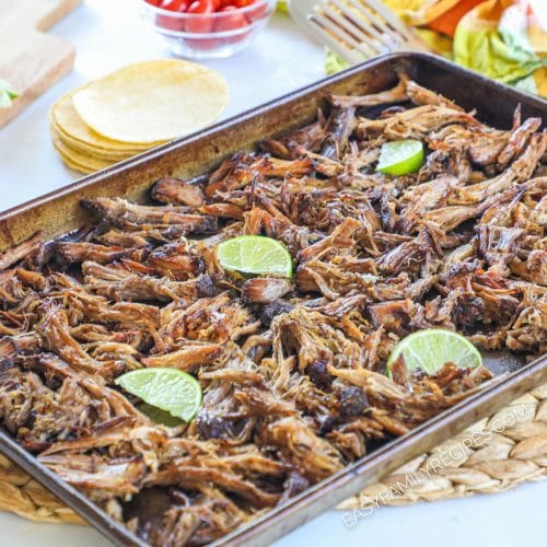 A baking sheet of shredded slow cooker carnitas with lime wedges