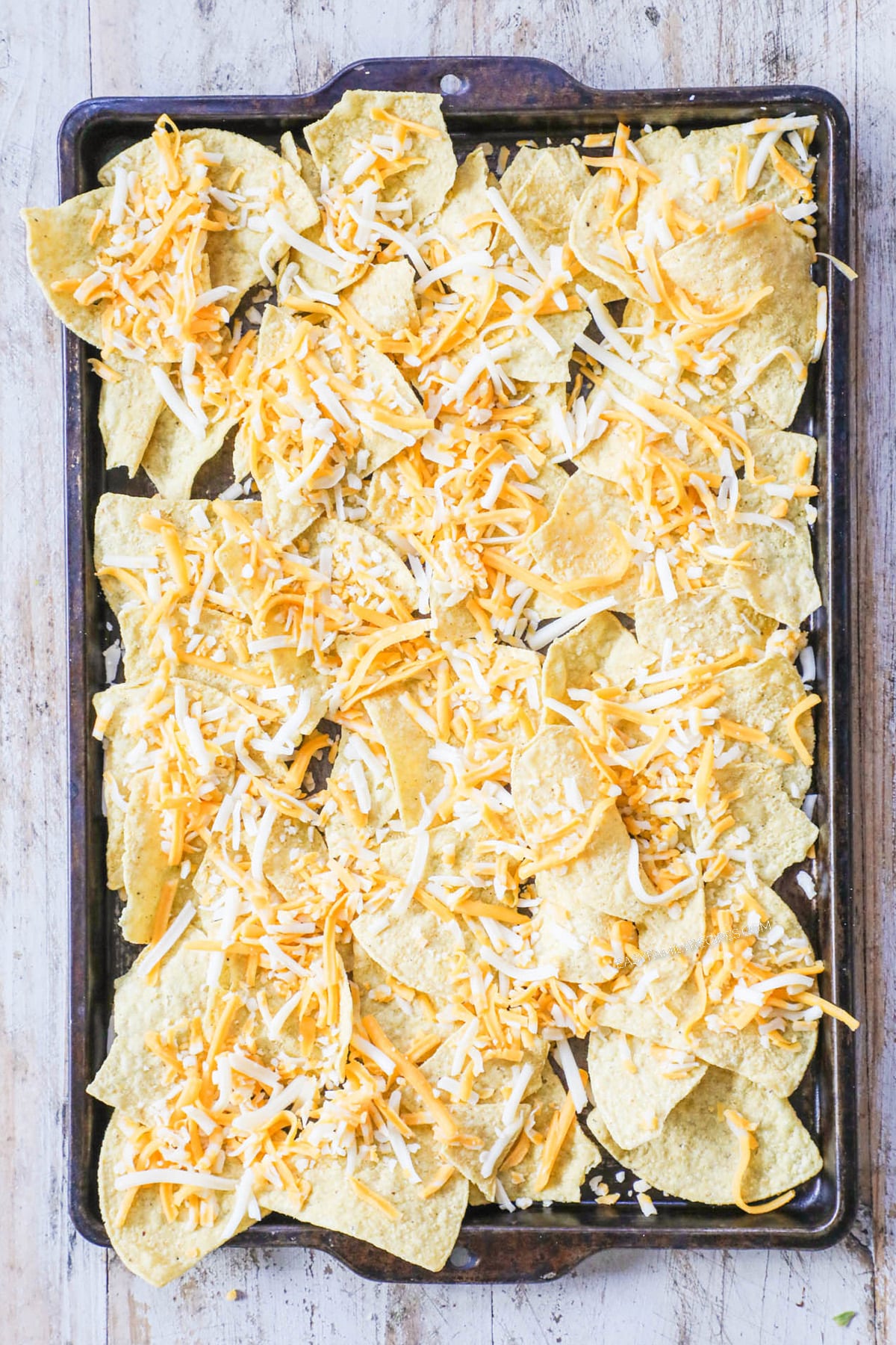 How to Make Carnitas Nachos: Step 1: Assemble the nachos and spread chips in layer over a large baking sheet. Top with 1/2 the cheese