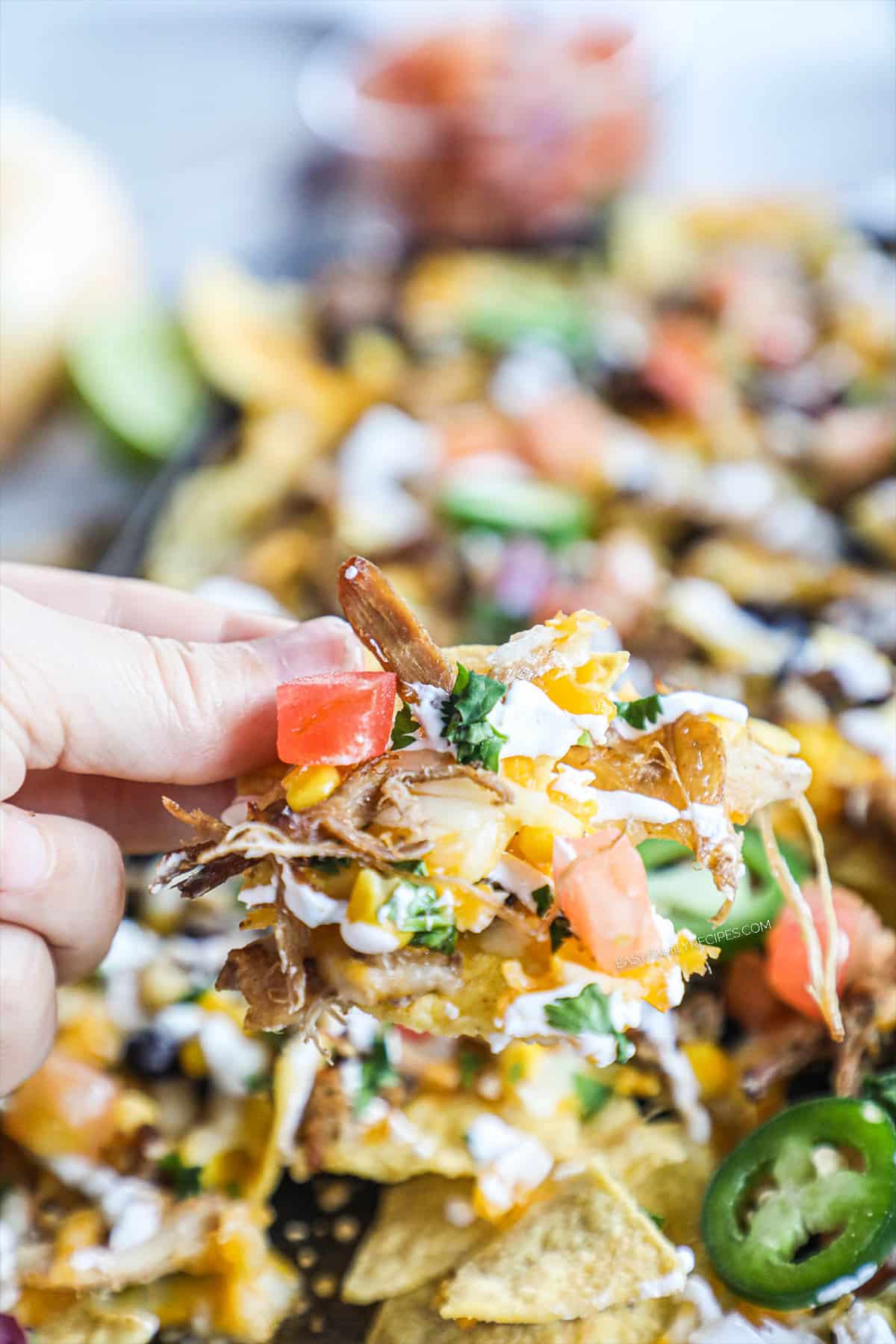 close up of hand picking up nachos with all ingredients loaded on chip