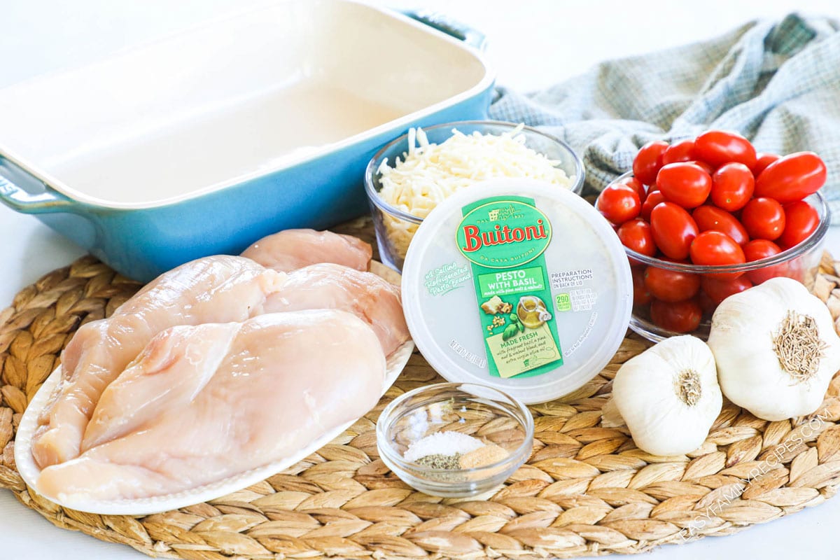 Ingredients to make a pesto chicken bake including chicken breasts, pesto, cherry tomatoes, mozzarella cheese, and garlic