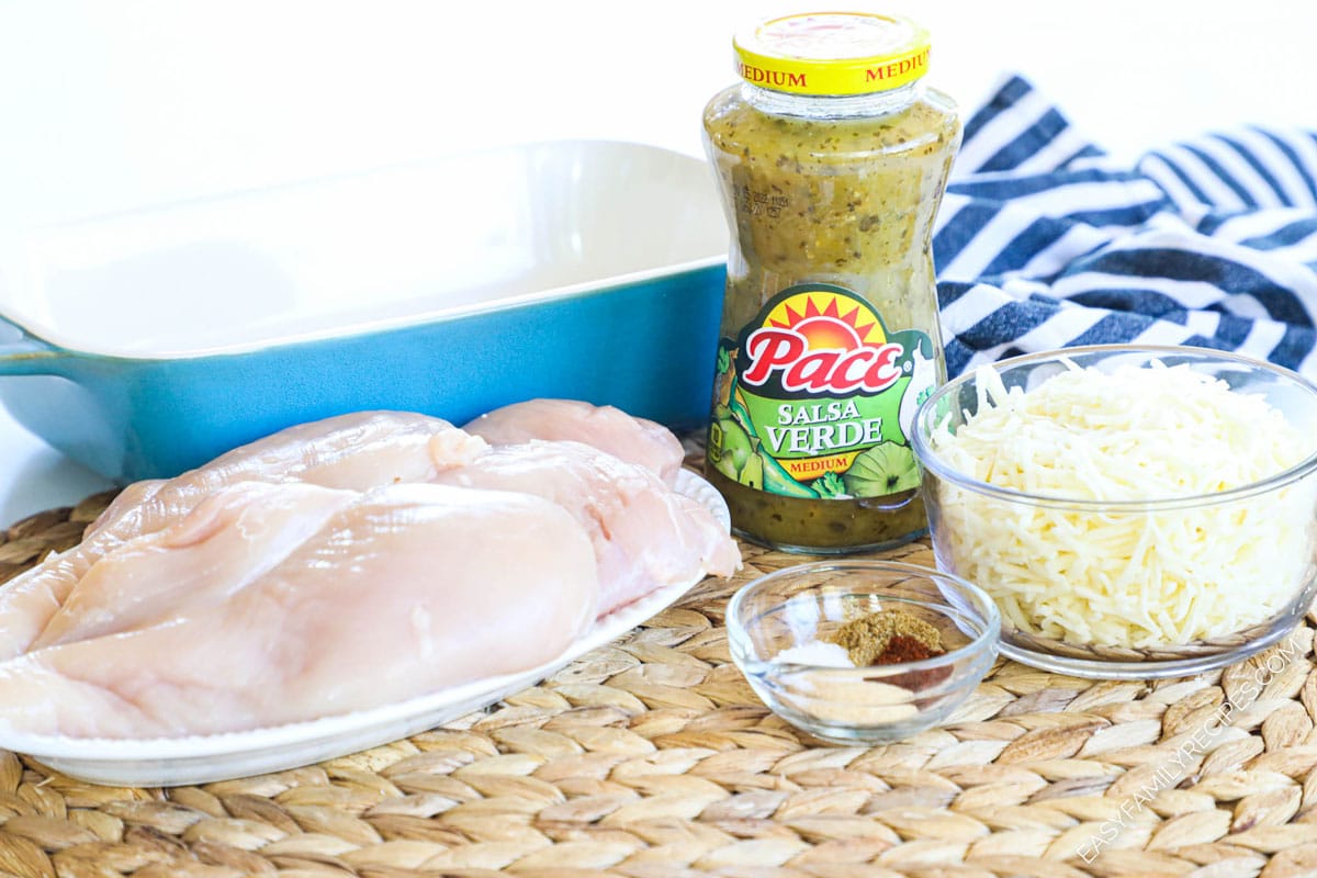 Ingredients for Salsa Verde Baked Chicken including chicken breasts, shredded cheese, spices, and Salsa Verde in a jar