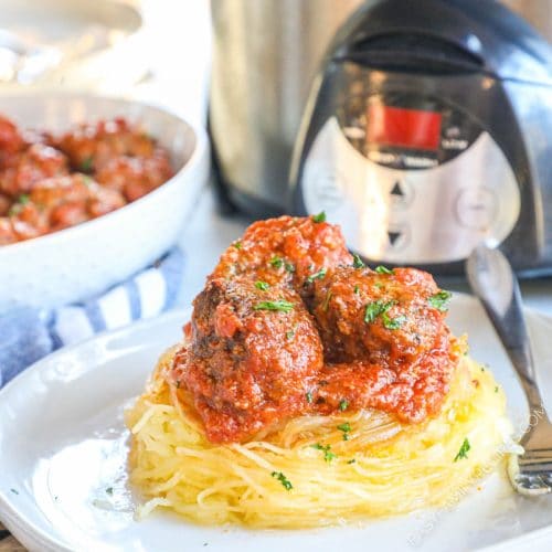 Spaghetti squash with meatballs and marinara sauce on top in front of a crock pot