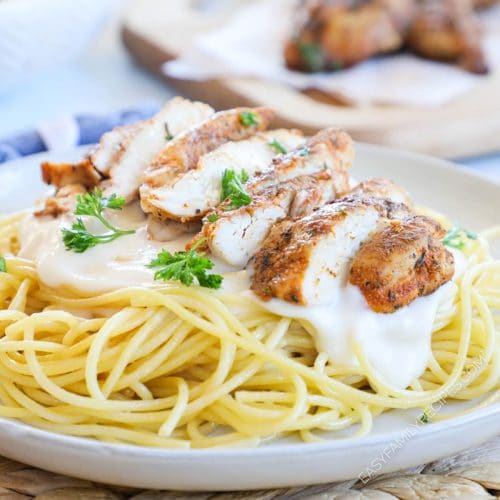 a plate of blackened chicken alfredo pasta topped with parsley