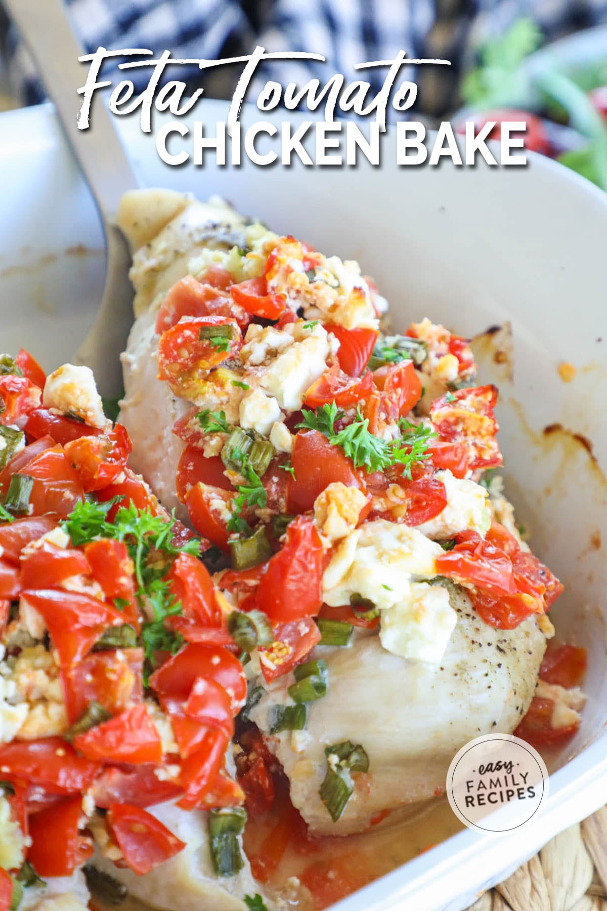 Chicken breast in pan being scooped out. Chicken breast is topped with feta, tomato, and green onions.