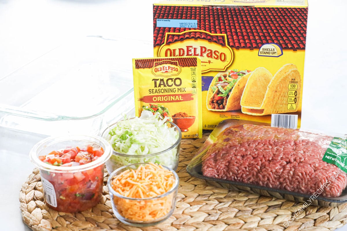 Ingredients for making baked crispy ground beef tacos including crispy taco shells, taco seasoning, ground beef, tomato sauce, shredded cheese, and shredded lettuce and salsa for toppings.