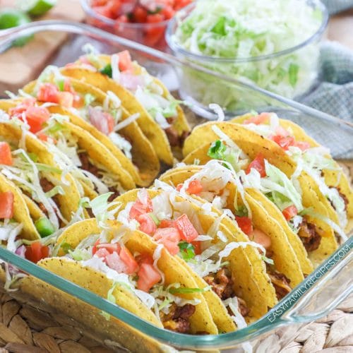 A tray of 10 tacos filled with beef, tomatoes, lettuce, and cheese.