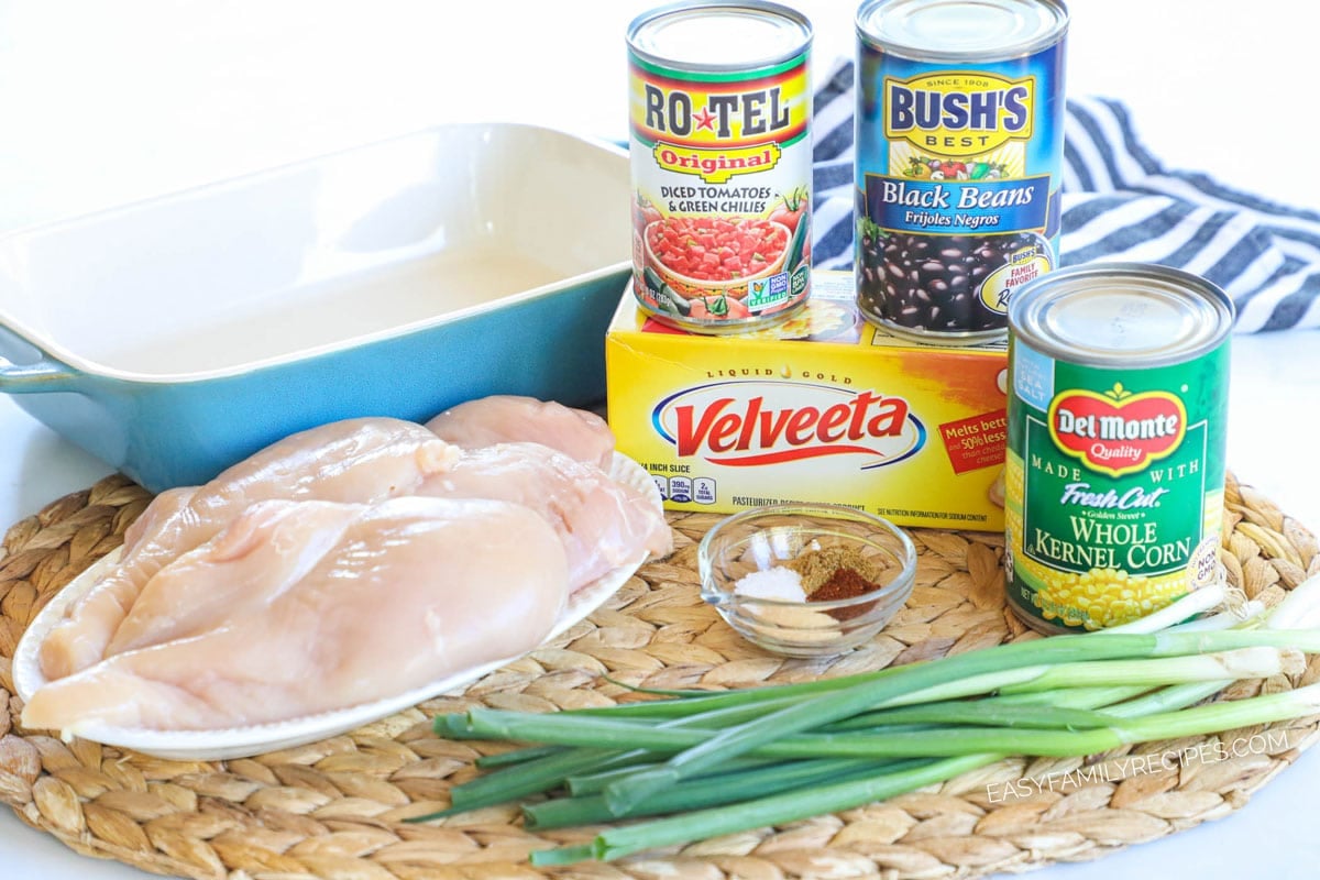 Ingredients for making queso chicken including Velveeta, canned corn, black beans, Rotel, and chicken breasts
