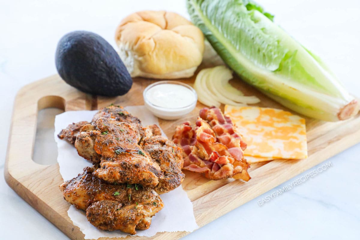 Ingredients for recipe: 2 pieces of blackened chicken filets, whole avocado, kaiser bun, cajun sandwich sauce, bacon, colby jack cheese slices, sliced onions, and romaine lettuce.