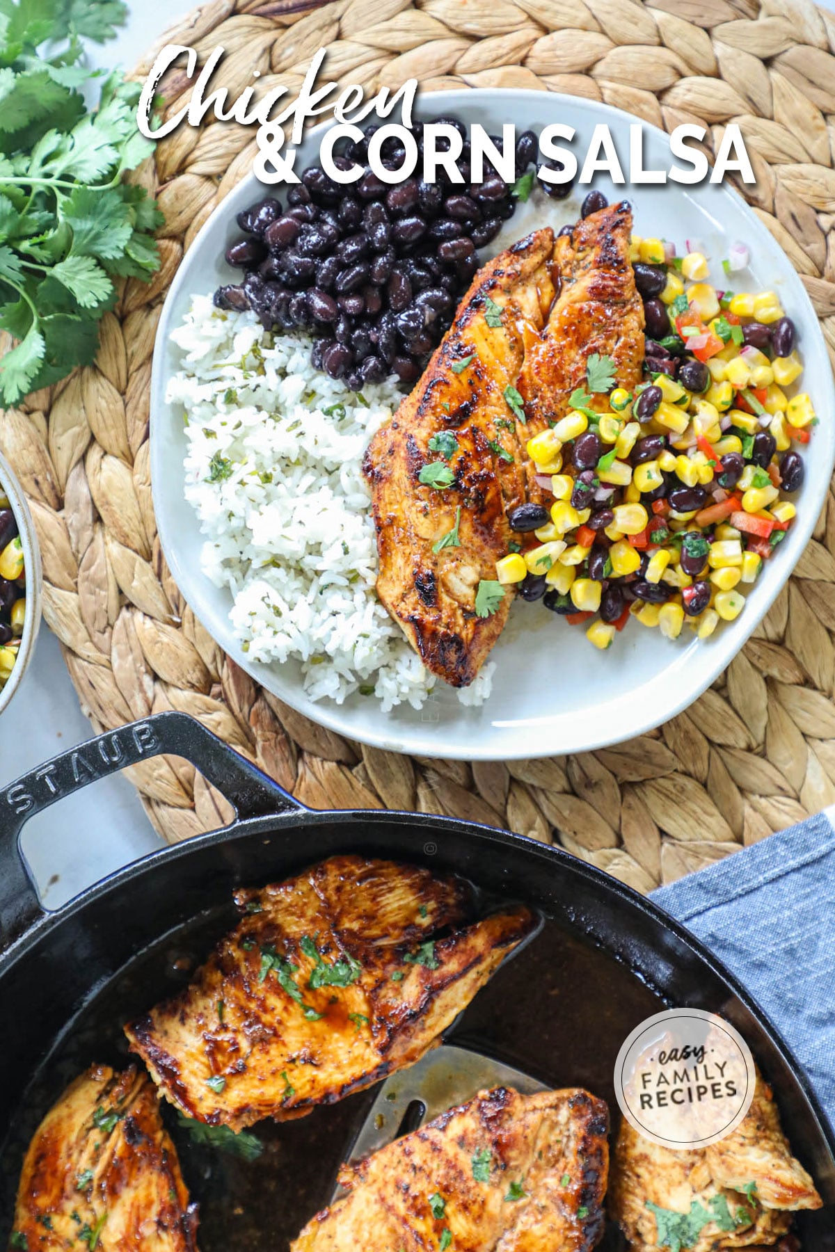 Seared chicken on a plate with corn salsa, black beans, and white rice with a skillet of chicken next to it.