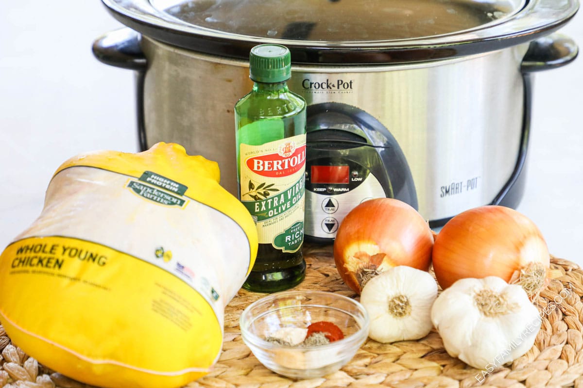 Ingredients to make Crock Pot rotisserie chicken including a whole chicken, spices, onion, and oil
