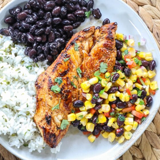 Seared chicken on a plate with corn salsa, black beans, and white rice.