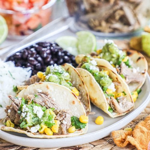 Side view of pork carnitas on large white plate served with a side of black beans and rice.