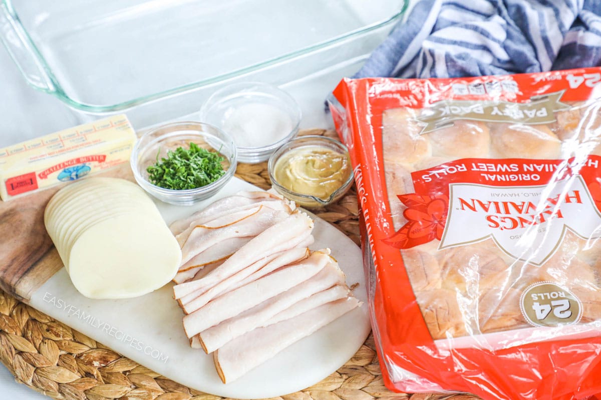 Ingredients for making turkey sliders including Hawaiian rolls, provolone cheese, turkey, parsley, butter, sugar, and dijon mustard.