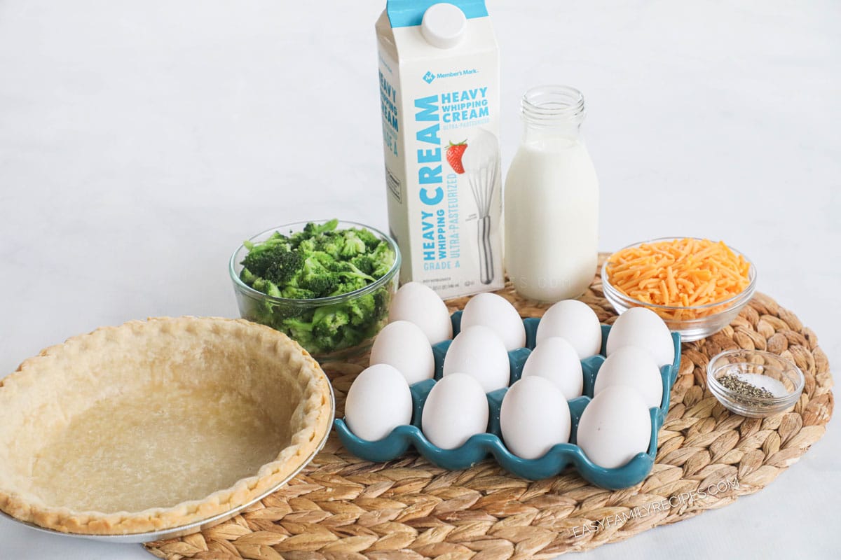 Ingredients for quiche including eggs, heavy cream, milk, broccoli, pie crust, cheddar cheese, and salt and pepper.