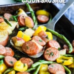 Spatula lifting smoked sausage, peppers, and green beans with cajun butter sauce.