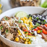 Ove head view of white bowl with pork carnitas, rice, black beans, corn limes, and red pepper. Drizzled with sour cream