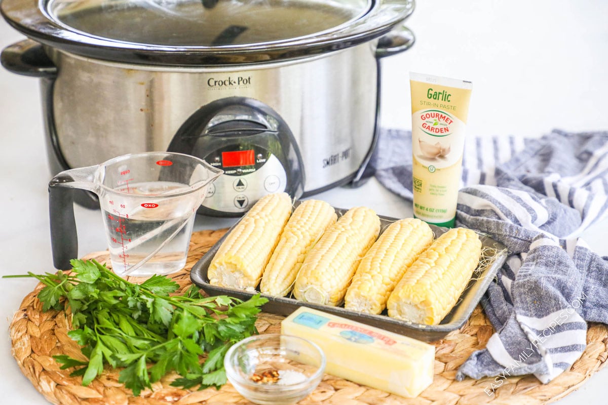 Ingredients for crock pot recipe: corn cobs, water, fresh herbs, garlic in a squeeze bottle, butter, and spices.