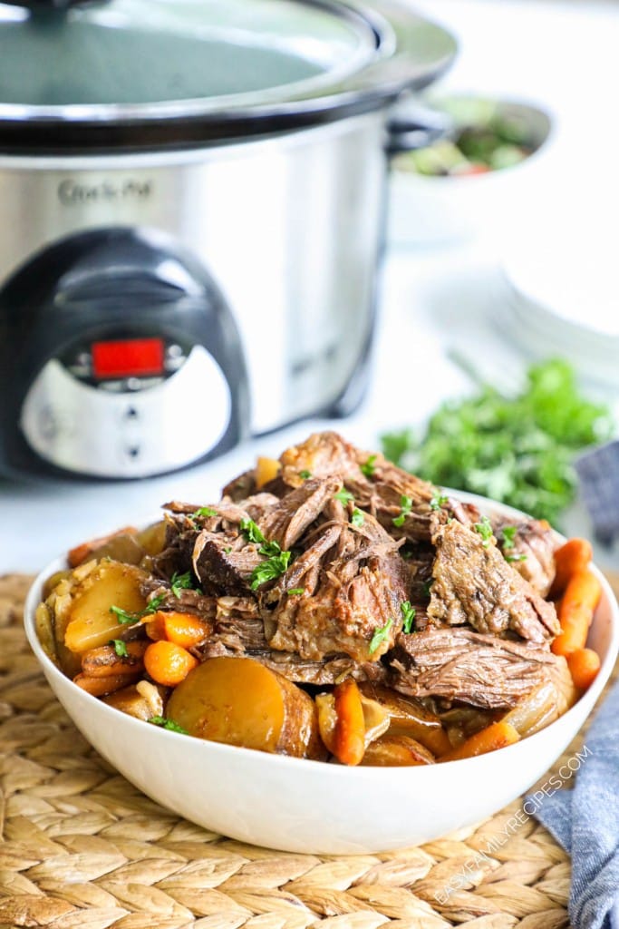 Pot roast with potatoes and carrots in a bowl in front of crockpot