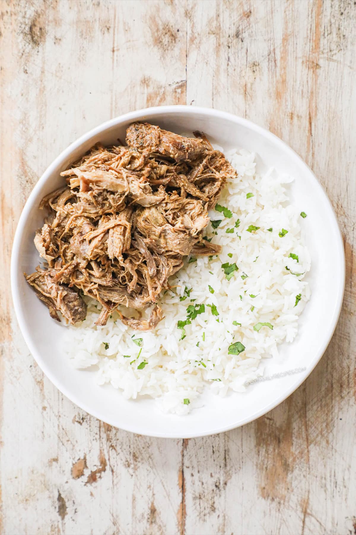 Step 2 of burrito bowl recipe - white bowl with pork carnitas and rice