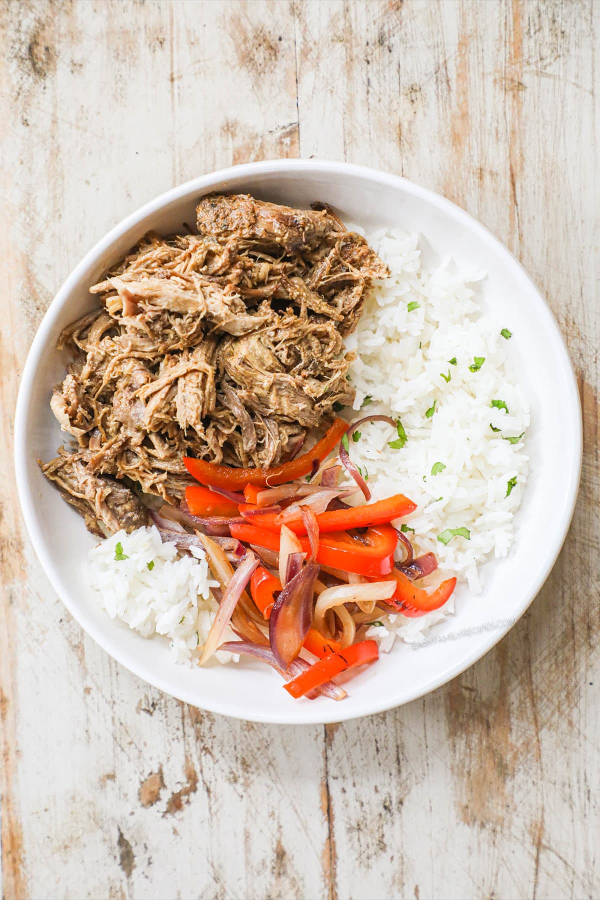 Step 3 of burrito bowl recipe - white bowl with pork carnitas, rice, onions and red pepper