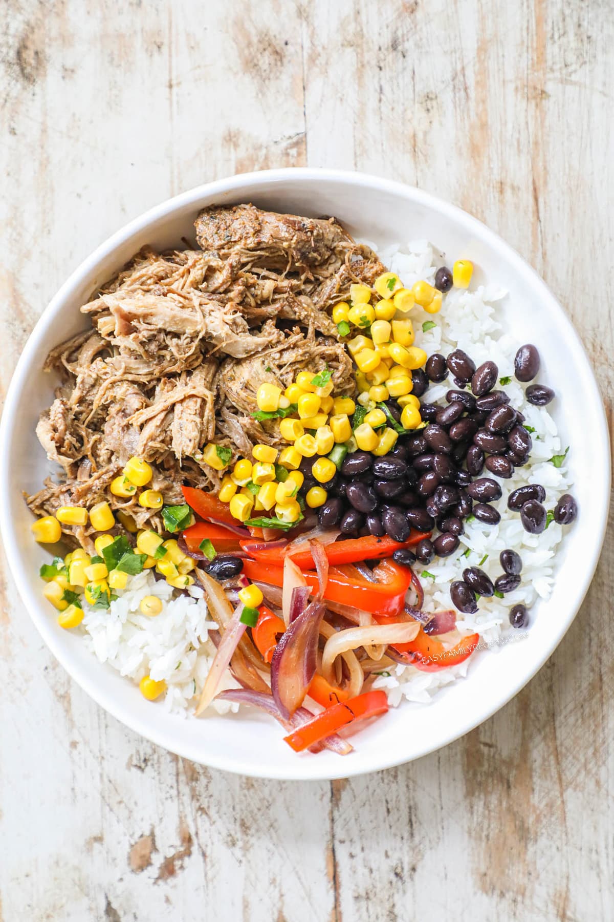 Step 4 of burrito bowl recipe - white bowl with pork carnitas, rice, black beans, corn, onion, limes, and red pepper