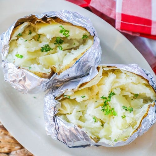 Two fluffy baked potatoes made in the Instant Pot Pressure cooker split open and resting on a plate
