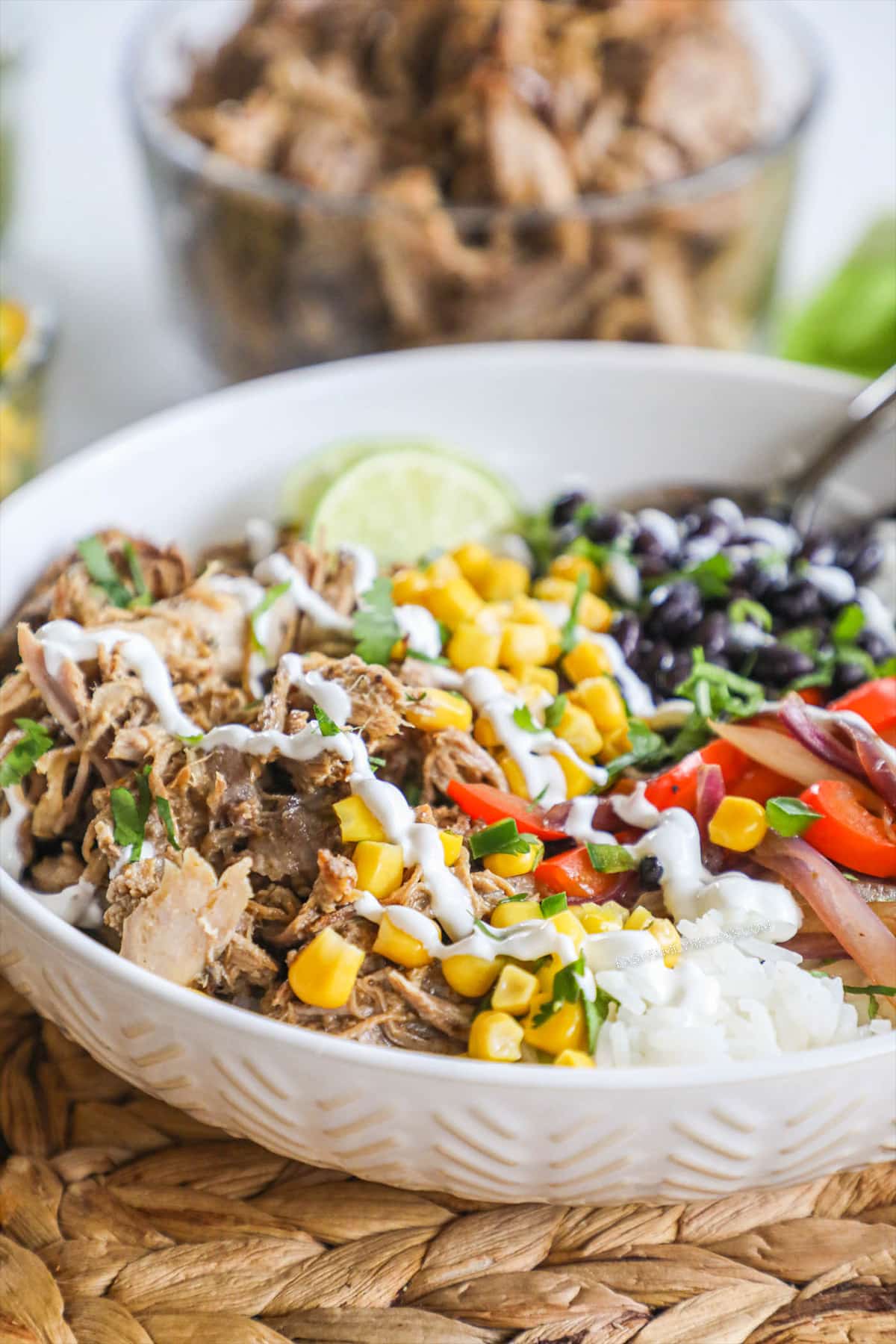 white bowl with pork carnitas, rice, black beans, corn limes, and red pepper