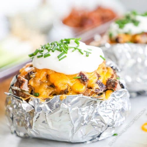 Close up of a baked potato in foil stuffed with chopped steak, cheese, sour cream, and chives.