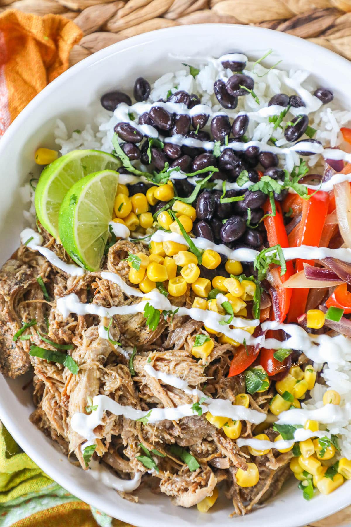 white bowl with pork carnitas, rice, black beans, corn limes, and red pepper