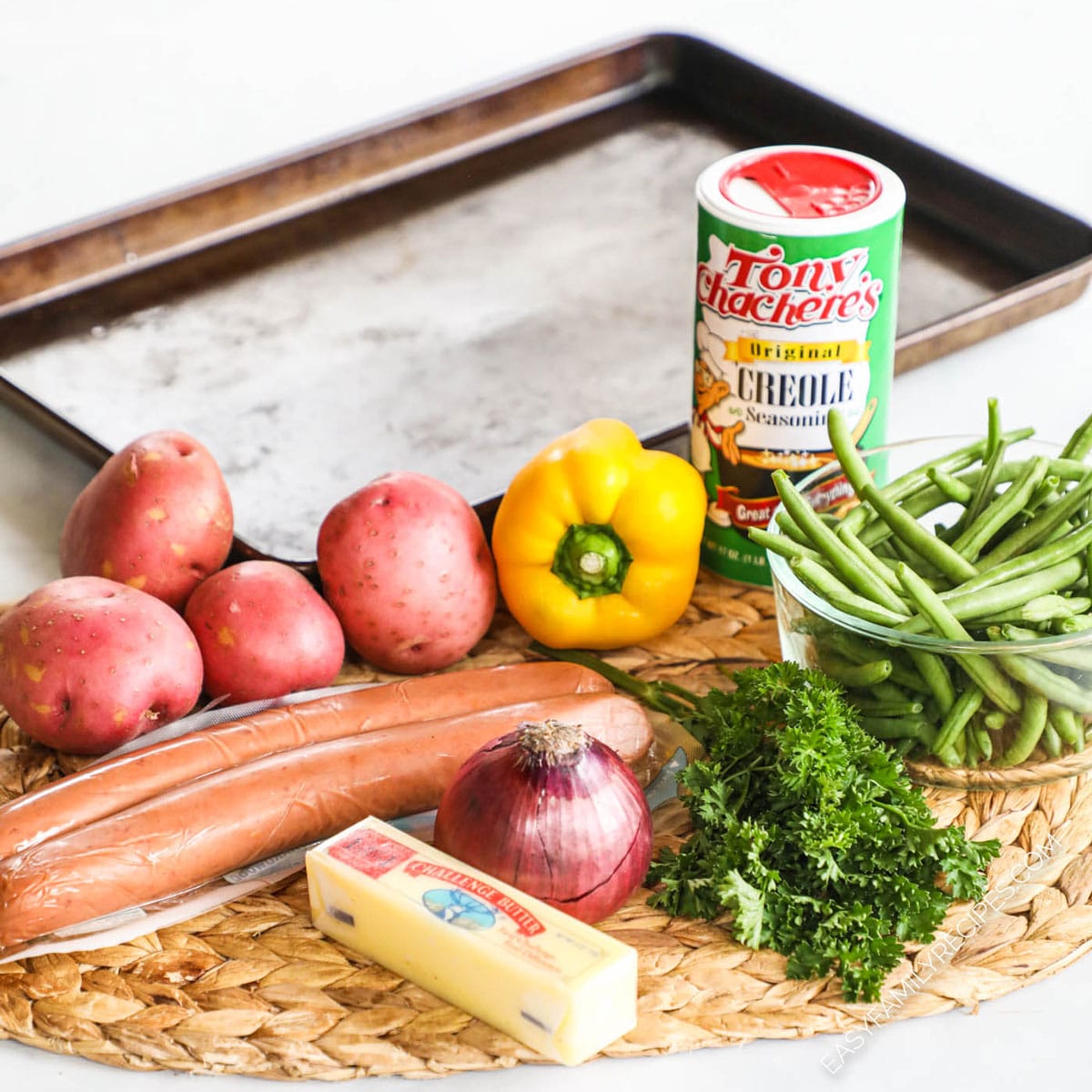 Ingredients to make sausage and potatoes sheet pan meal including cajun seasoning, green beans, potatoes, bell pepper, parsley, red onion, and butter.