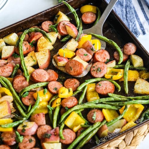 A spatula scooping out sausage and potatoes from sheet pan.