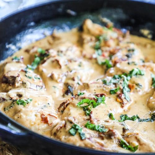 close up of the chicken in a cream sauce with fresh basil in a skillet.