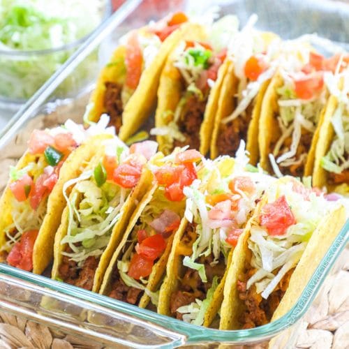 Ground turkey tacos in a baking dish with lettuce and tomatoes on top.