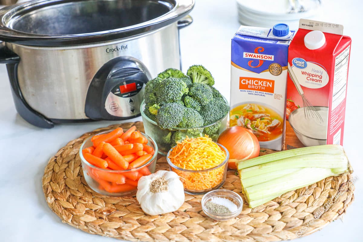 Ingredients to make Crock Pot Broccoli cheese soup including cheddar cheese, carrots, broccoli, celery, stock, and garlic.