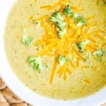 a bowl of creamy broccoli cheese soup topped with cheddar and broccoli.