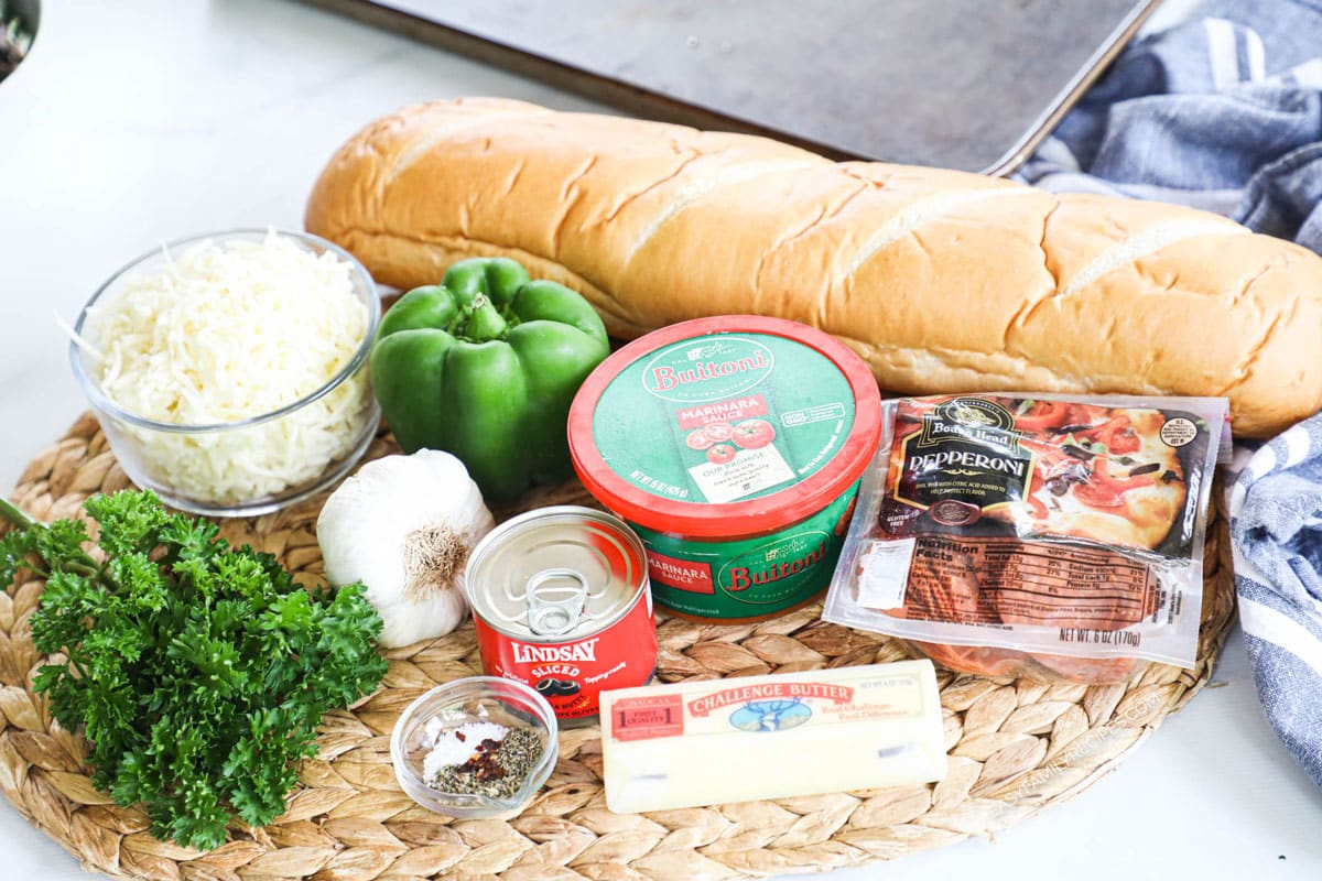 Ingredients to make garlic bread pizza including french bread, marinara sauce, mozzarella cheese, and pizza toppings.