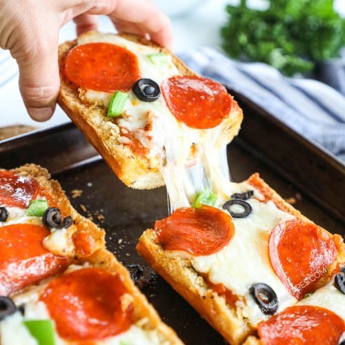 Lifting a slice of garlic bread pizza with pepperoni and olives from baking sheet with a big cheese pull