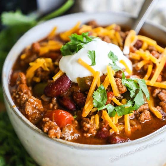 A bowl of thick and chunky beef and bean chili topped with cheese and sour cream.