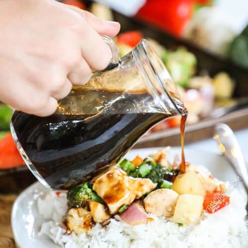 Teriyaki sauce being poured over chicken recipe with rice from a glass carafe.
