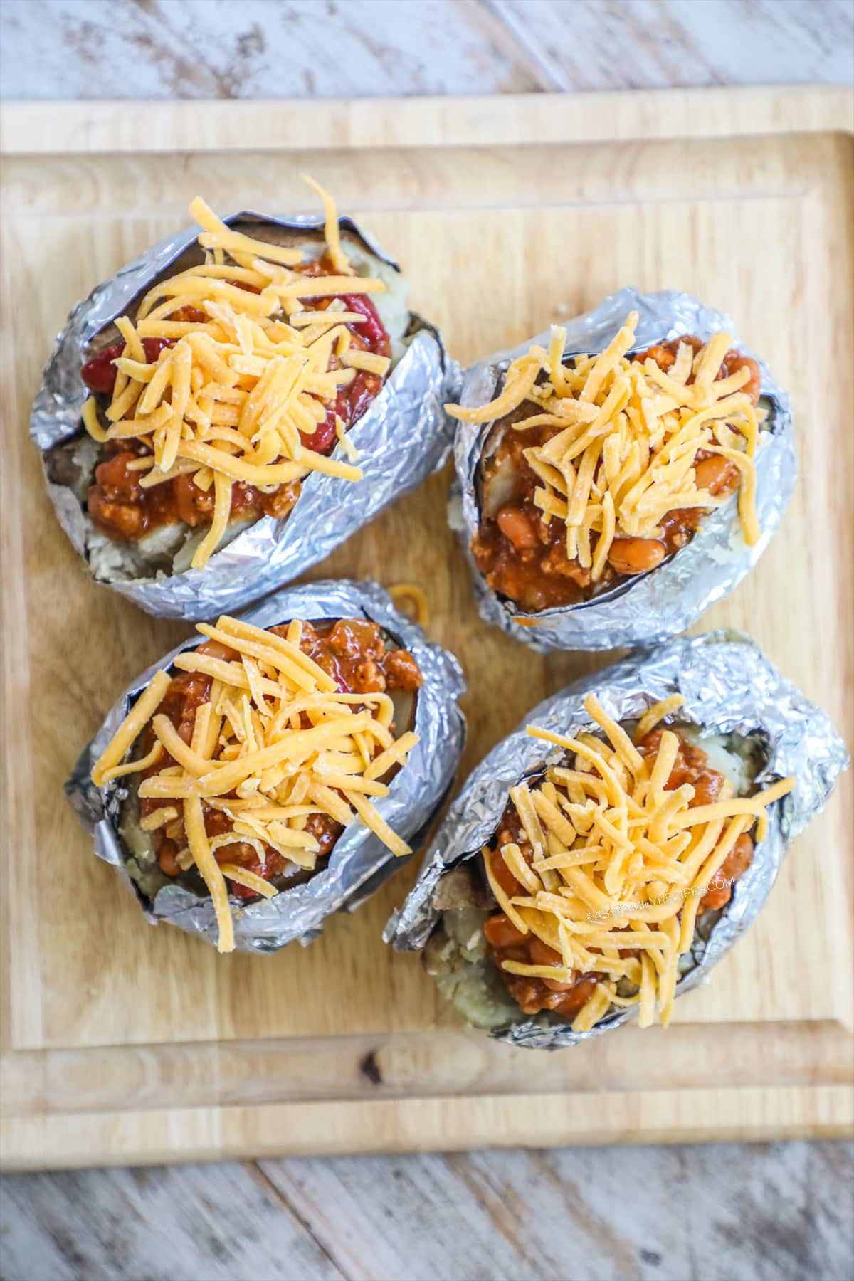 Step 3 of chili stuffed baked potatoes - top baked potato with cheese which goes on top of the chili and bacon