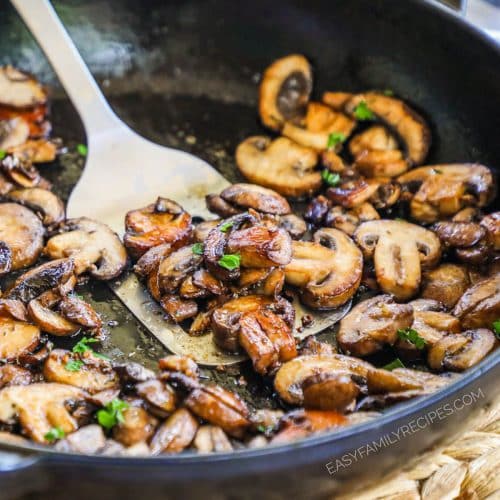 Close up of sauted mushrooms with a metal spatula scooping some up.