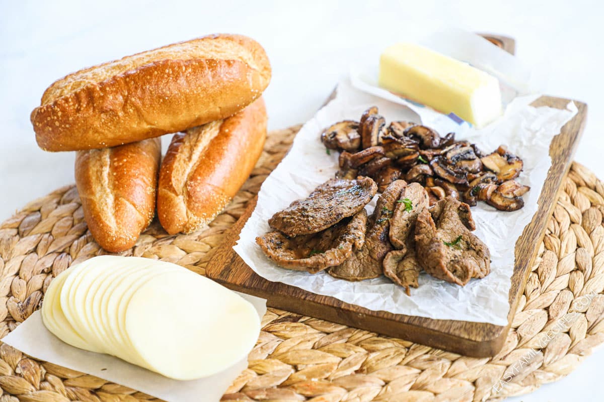 Ingredients for steak sandwich including mushrooms, steak, provolone, butter, bread, and seasonings.